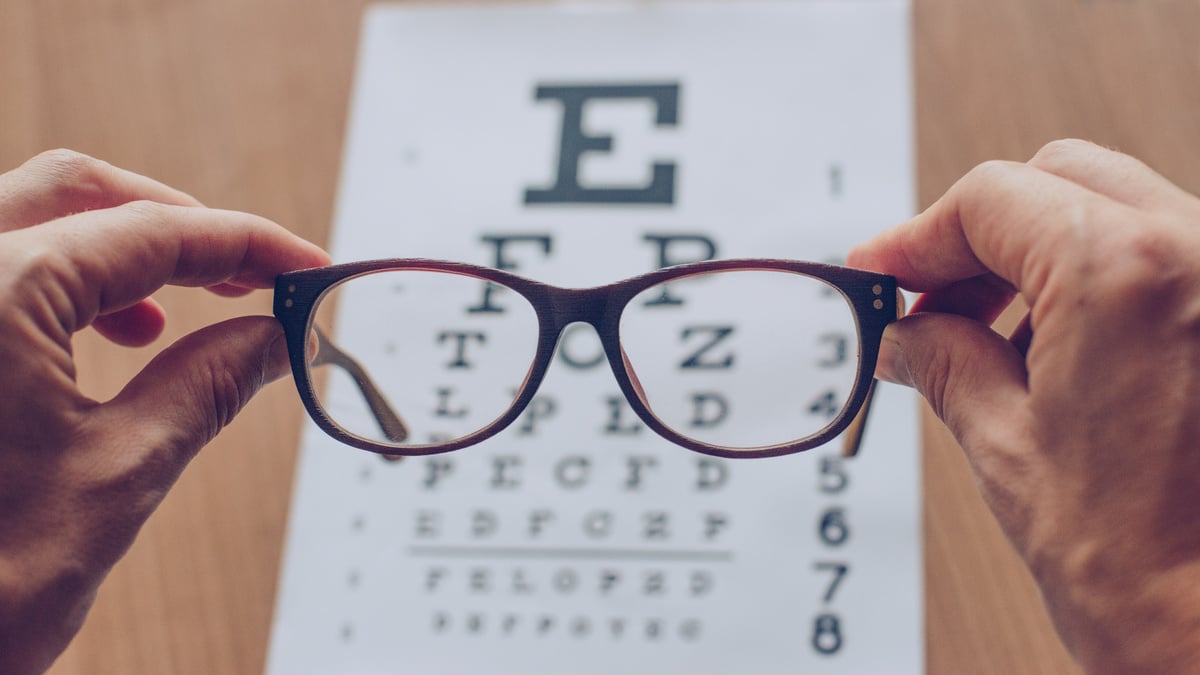 Hands holding sight glasses in front of optician sight chart. Eyesight optician concept